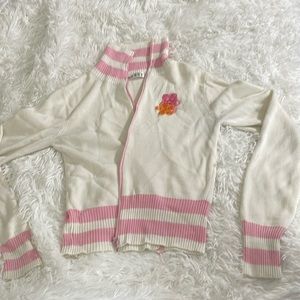White sweater with pink and orange flowers, and has 2 white stripes on sleeves.
